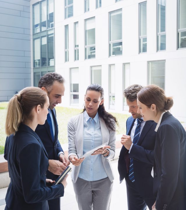 Businesspeople discussing over digital tablet outside office building Businesspeople discussing over digital tablet outside office building